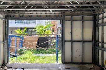 View through an unfinished wall shows outdoor greenery and urban structures.
