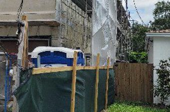 Construction site with scaffolding and protective coverings beside a green lawn.