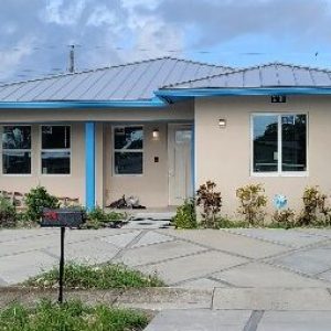 Single-story house with a blue roof and beige walls under a cloudy sky.