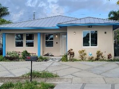 Single-story house with a blue roof and beige walls under a cloudy sky.