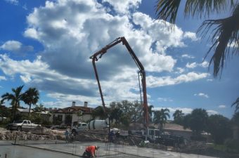 Construction workers and machinery work under a blue sky with large clouds.