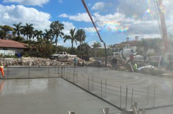 Freshly poured concrete slab at a sunny construction site with palm trees.