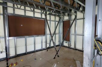 Interior view of a metal-framed room under construction with drywall panels.