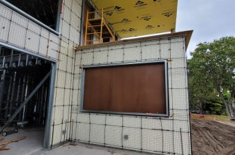 Unfinished outdoor wall with a large recessed brown panel.