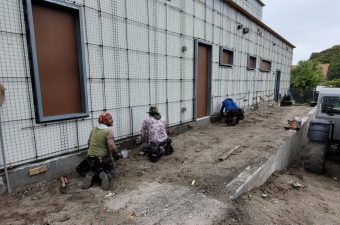Three people gardening next to a building wall.