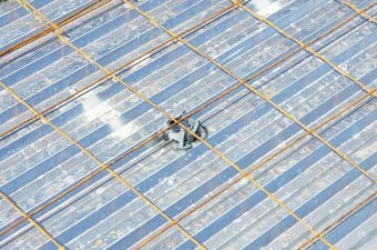 Worker installing solar panels on a large roof under a sunny sky.