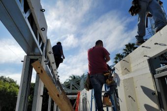 Construction workers building a structure under a partly cloudy sky.