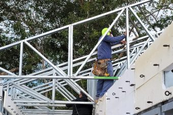 Worker installing metal framework on a building roof with safety gear.