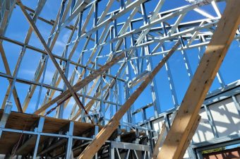 Wooden and metal trusses forming a roof structure under a clear blue sky.