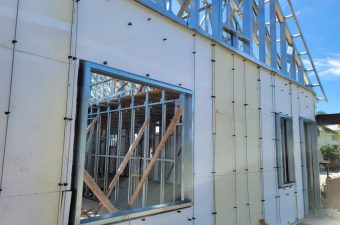Construction site showing a building's exterior wall with a window frame and wooden supports.