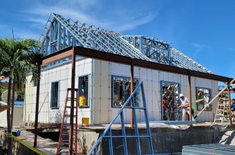House under construction with workers on site and steel framework.