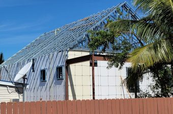 A house under construction with a unique triangular roof and palm trees nearby.