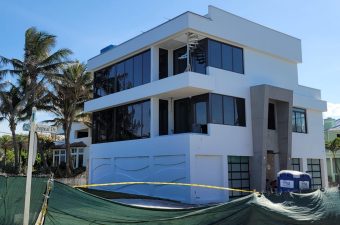 Modern white three-story building under construction with palm trees nearby.