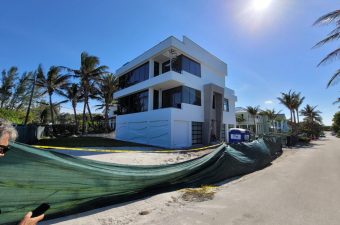 Modern white house under construction with palm trees and clear sky.