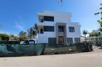 Modern two-story house under clear blue sky with surrounding palm trees.