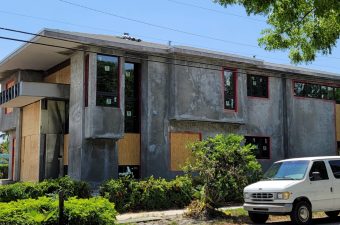 A house under renovation with boarded windows and a car parked outside.