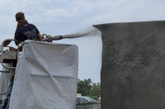 Worker spraying concrete onto a vertical surface for construction.