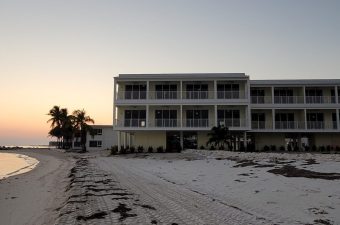 A modern beachfront building at sunset with palm trees and sandy shore.