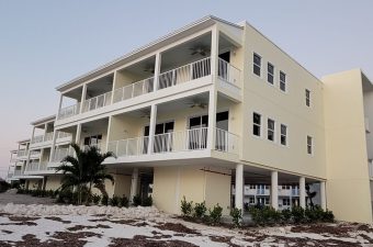 A modern three-story yellow house with large balconies and palm trees.
