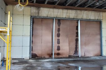 Three large copper panels with vertical dark spots in an indoor industrial space.