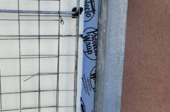 A partially tiled wall with a strip of blue waterproof membrane.