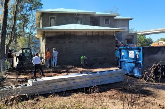 Workers renovating the exterior wall of a two-story house on a sunny day.