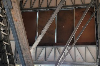 Metal beams and girders supporting a roof structure with sunlight streaming through.