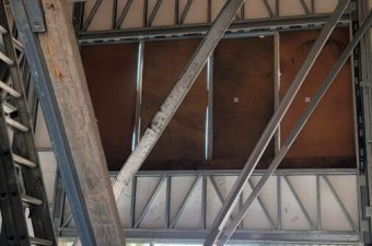 Metal beams and girders supporting a roof structure with sunlight streaming through.