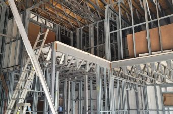 Interior view of building under construction with exposed steel framing and wooden ceiling.