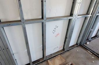 Construction site wall with metal studs and a white panel labeled 'C2X'.