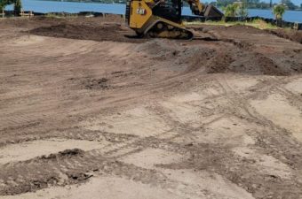 A bulldozer leveling dirt on a construction site near water.