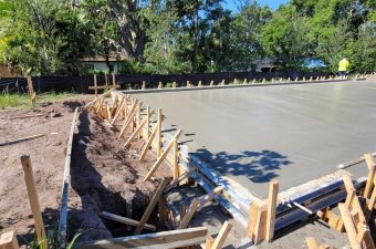 Freshly poured concrete slab with wooden supports in a sunny outdoor setting.