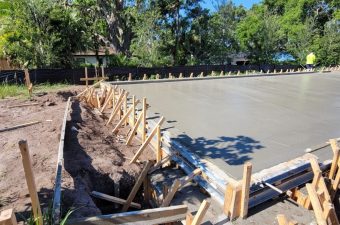 Freshly poured concrete slab with wooden supports in a sunny outdoor setting.