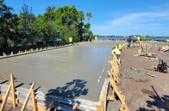 Workers pouring and leveling concrete near a waterfront.