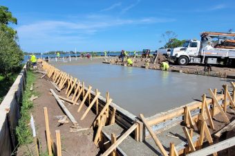 Workers pouring and smoothing concrete on a sunny construction site.
