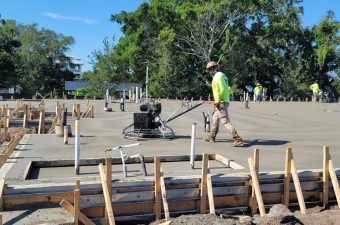 Construction worker walking on a site with concrete equipment and wooden frames.