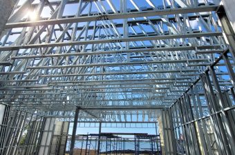 Steel framework of a building under construction with a clear blue sky.