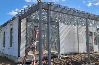 Construction site with steel framework and concrete walls under a blue sky.