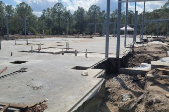 Concrete foundation slab being poured at a construction site with steel columns installed.
