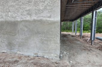 Unfinished concrete building with exposed columns and dirt ground.