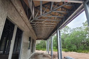 View of a building under construction showing metal roof trusses and steel columns.