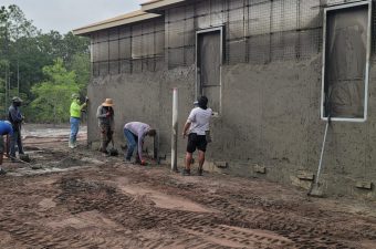 Workers plastering an exterior wall of a building under construction.