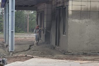 A man plastering a building wall outdoors.