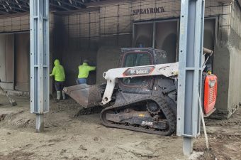 Workers load material into a tracked loader inside a warehouse.