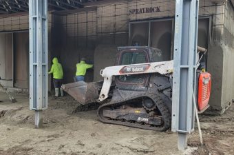 Workers load material into a tracked loader inside a warehouse.
