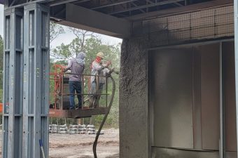 Two workers spraying concrete onto a wall inside a construction site.
