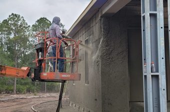 Worker applying plaster to a building exterior using a lift.