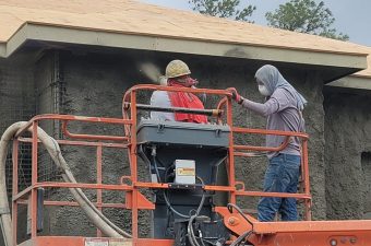 Two men working on scaffolding near a building wall.