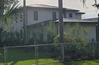 A residential house with a fenced yard and greenery.