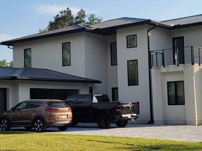 Modern white house with multiple large windows and parked cars.